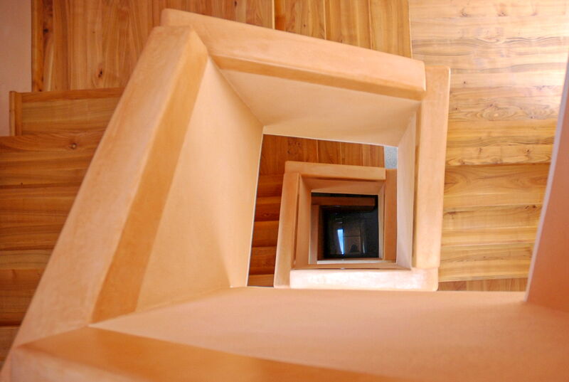 View into the stairwell with natural lime plaster in warm tones and wooden staircase