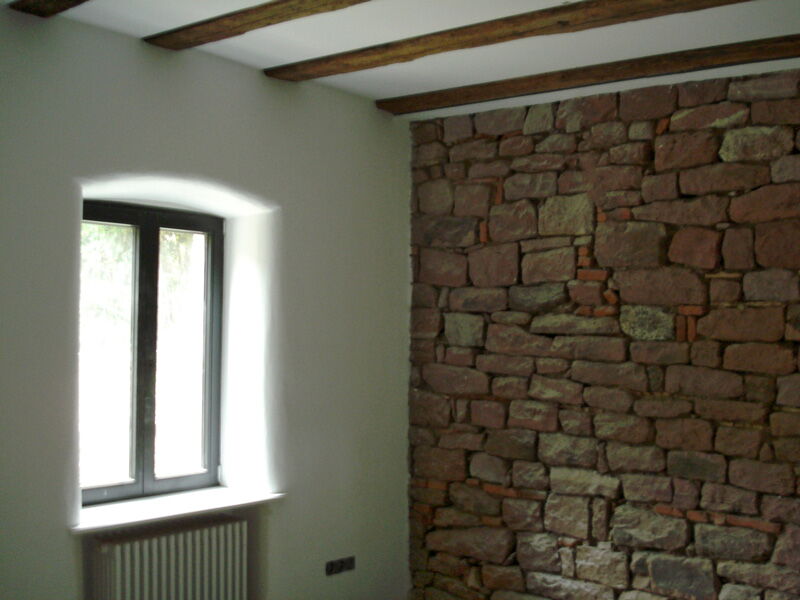 Interior room with white natural lime plaster, exposed wooden beams and natural stone wall