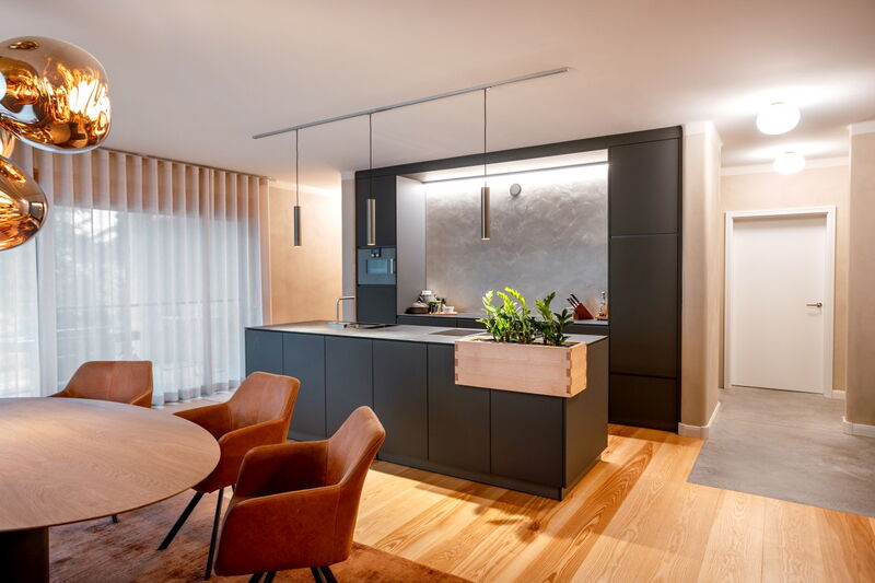 Modern living space with black kitchen island and grey natural lime plaster wall with indirect lighting