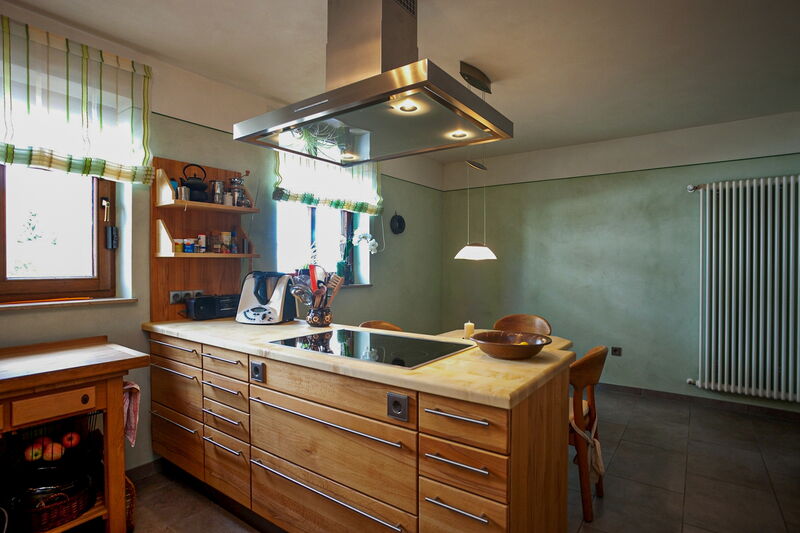 Kitchen with island, wooden cabinetry and green natural lime plaster wall