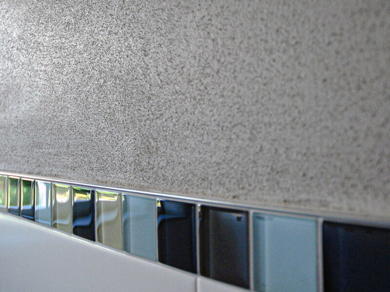 Close-up of grey natural lime plaster above tiles with mosaic border