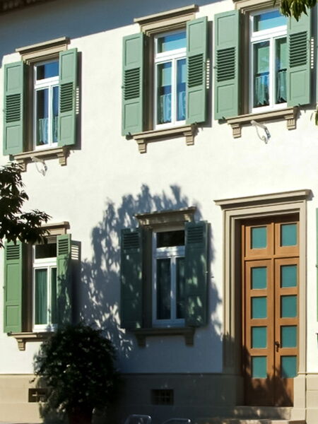 Natural lime plaster facade with green shutters and entrance door