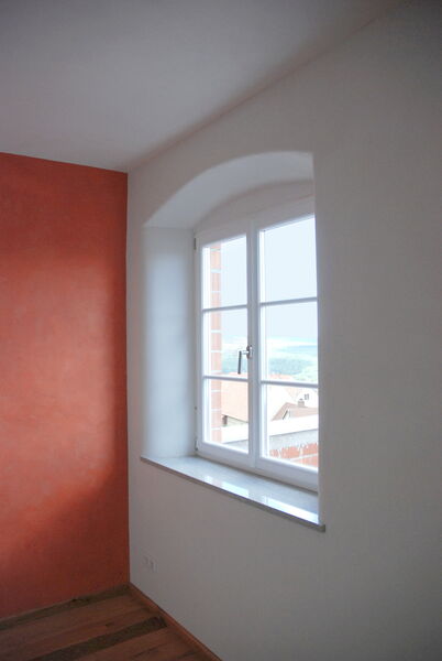 Room with red natural lime plaster and arched window with a view